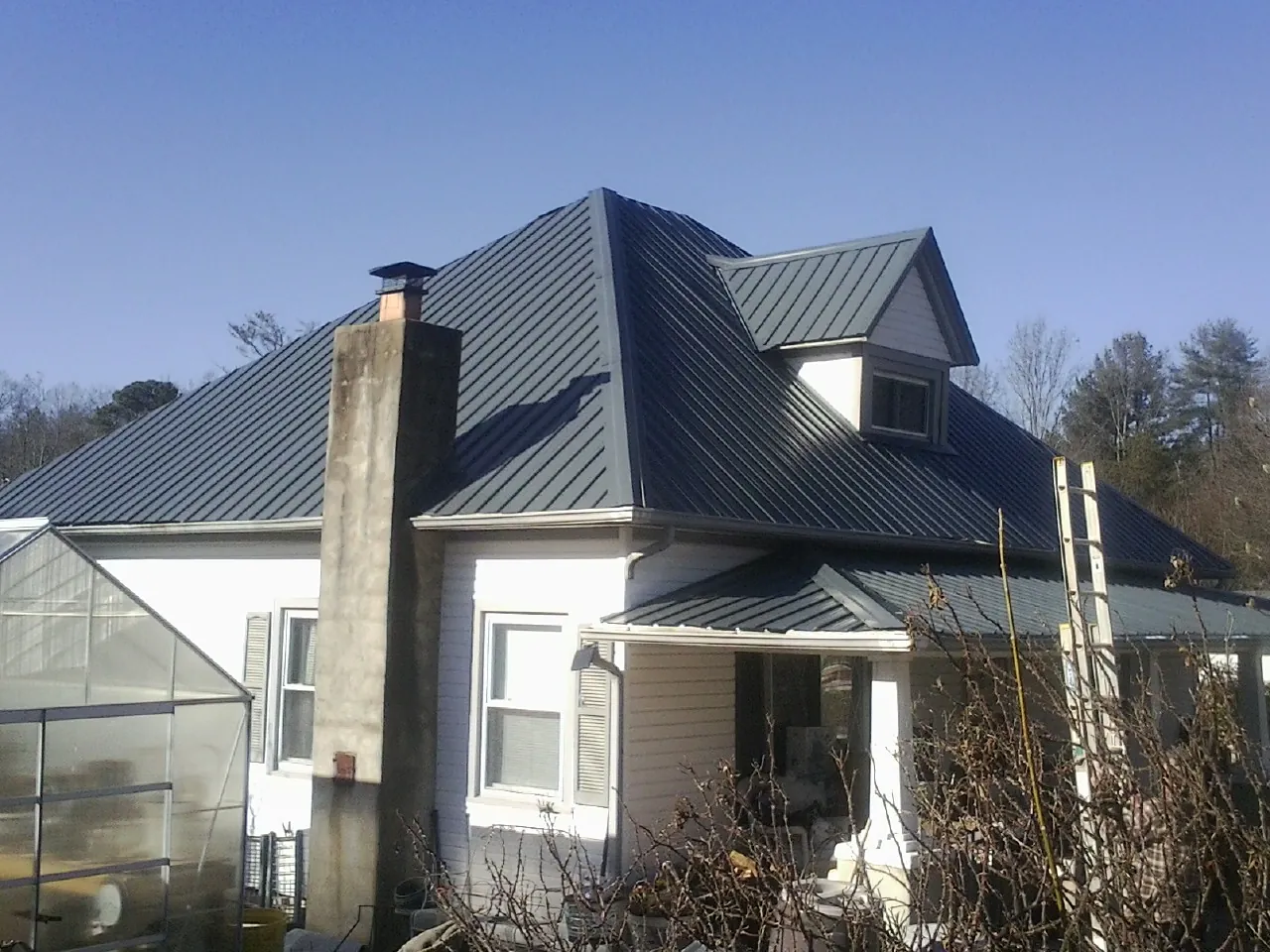 Dark blue standing seam metal roof on a white farmhouse with dormer — Slate & Tile Roof Repair by Roofing Brothers in Fischer