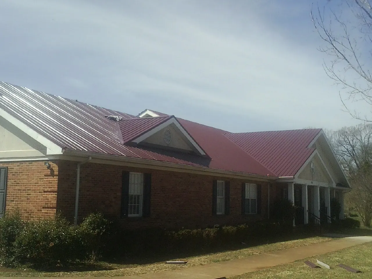 Red metal roof with gabled entries on a long brick building, from a Hail Damage Roof Repair job in Fischer