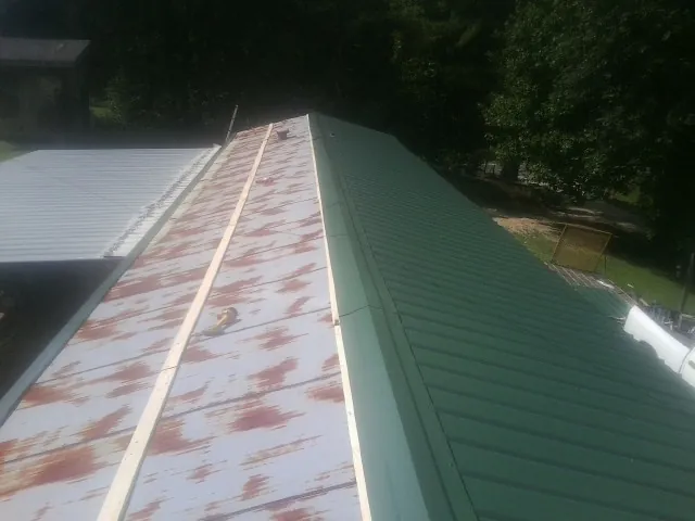 Old rusted panels beside newly installed green metal roofing — Wind Damage Roof Repair by Roofing Brothers in Fischer