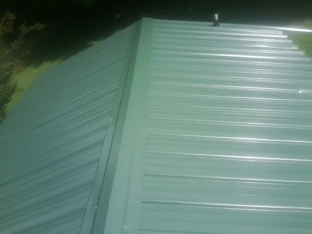New green metal panels meeting at the ridge of a roof — Flat Roof Repair work by our crew in Fischer