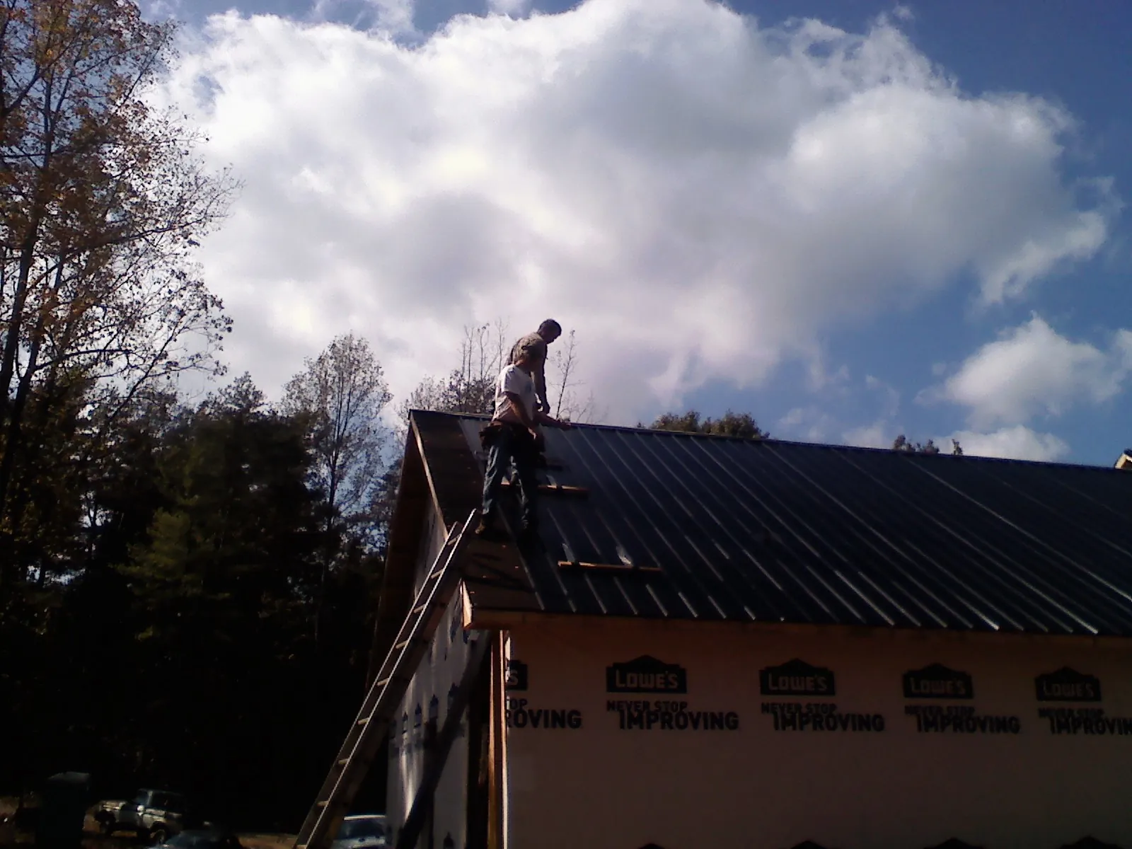 Roofer fastening dark metal panels high against a cloudy sky, from a Roof Inspection job in Fischer
