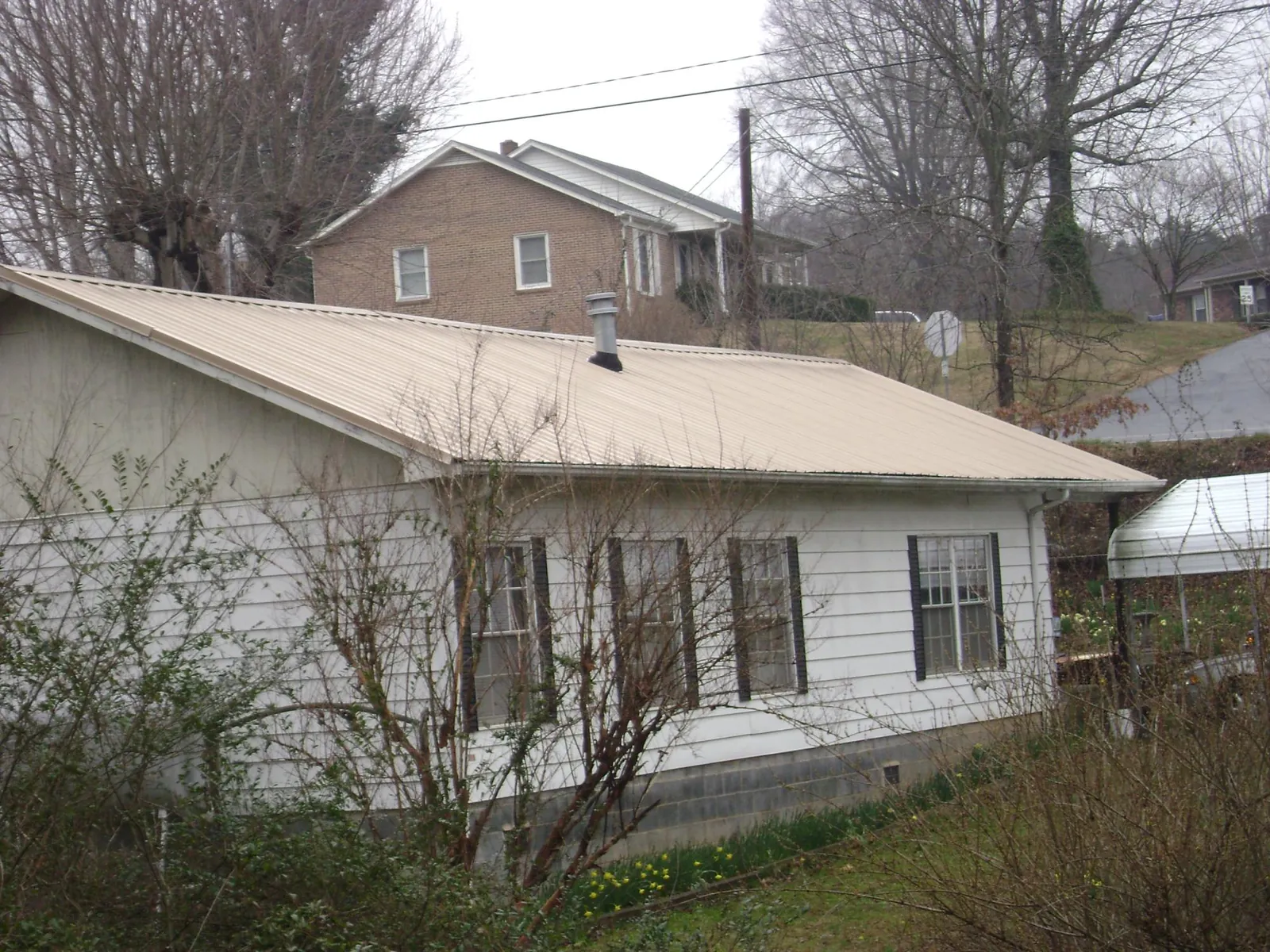 Tan metal roof on a white sided house set into a hillside — Commercial Roofing by Roofing Brothers in Fischer